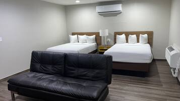A hotel room with two beds, a black leather sofa, and an air conditioning unit.