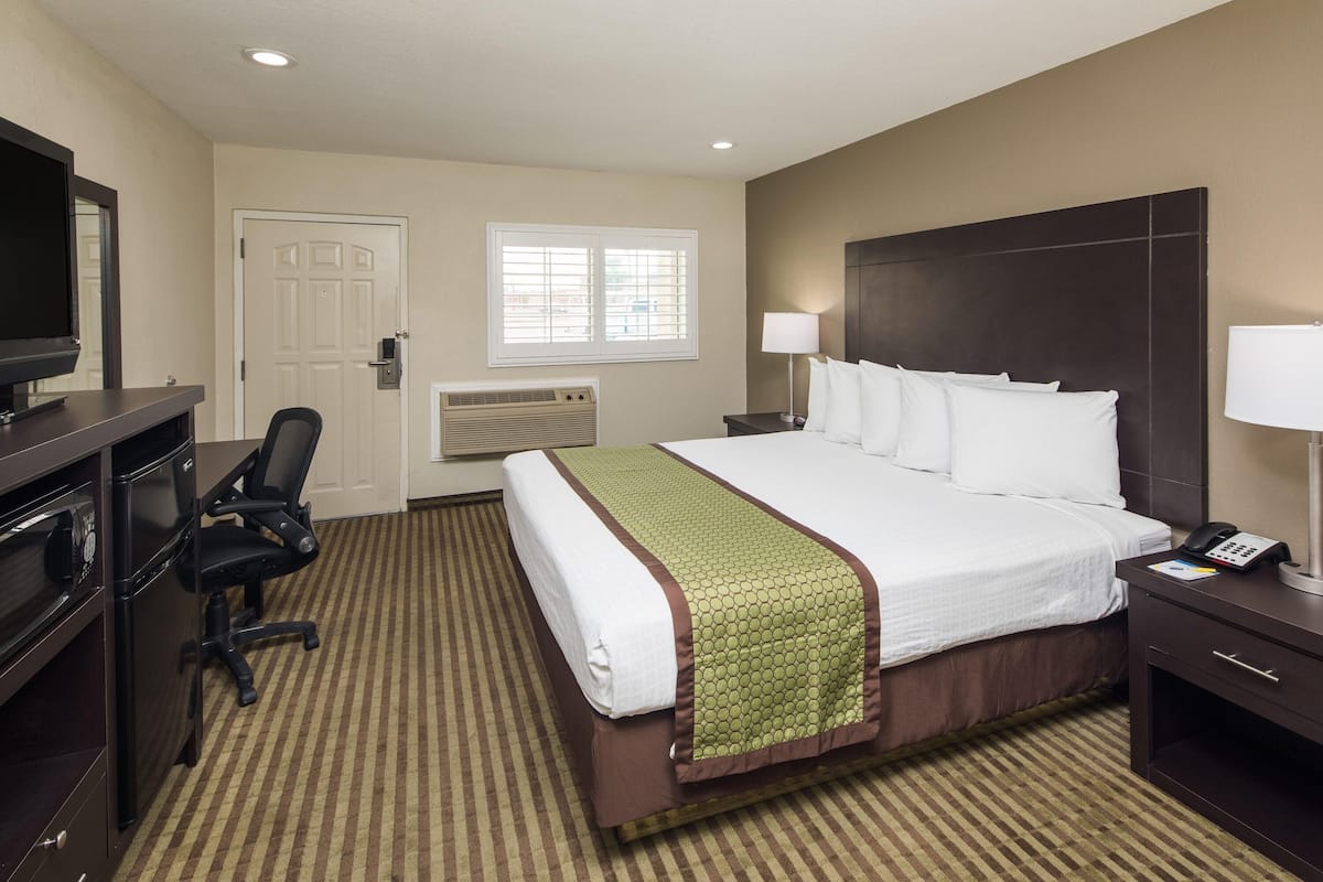 A hotel room with a bed, a desk with a TV, a chair, a window, and a lamp.