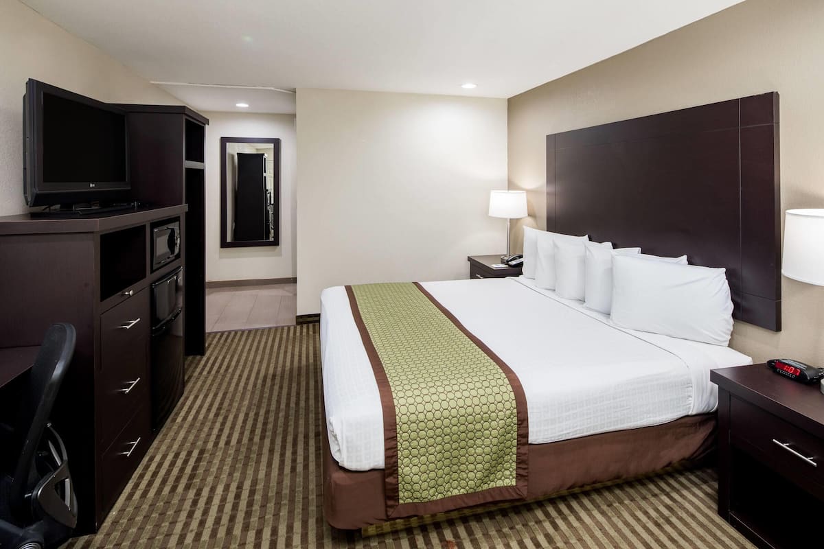 A hotel room with a bed, a desk, a TV, a lamp, and a mirror.