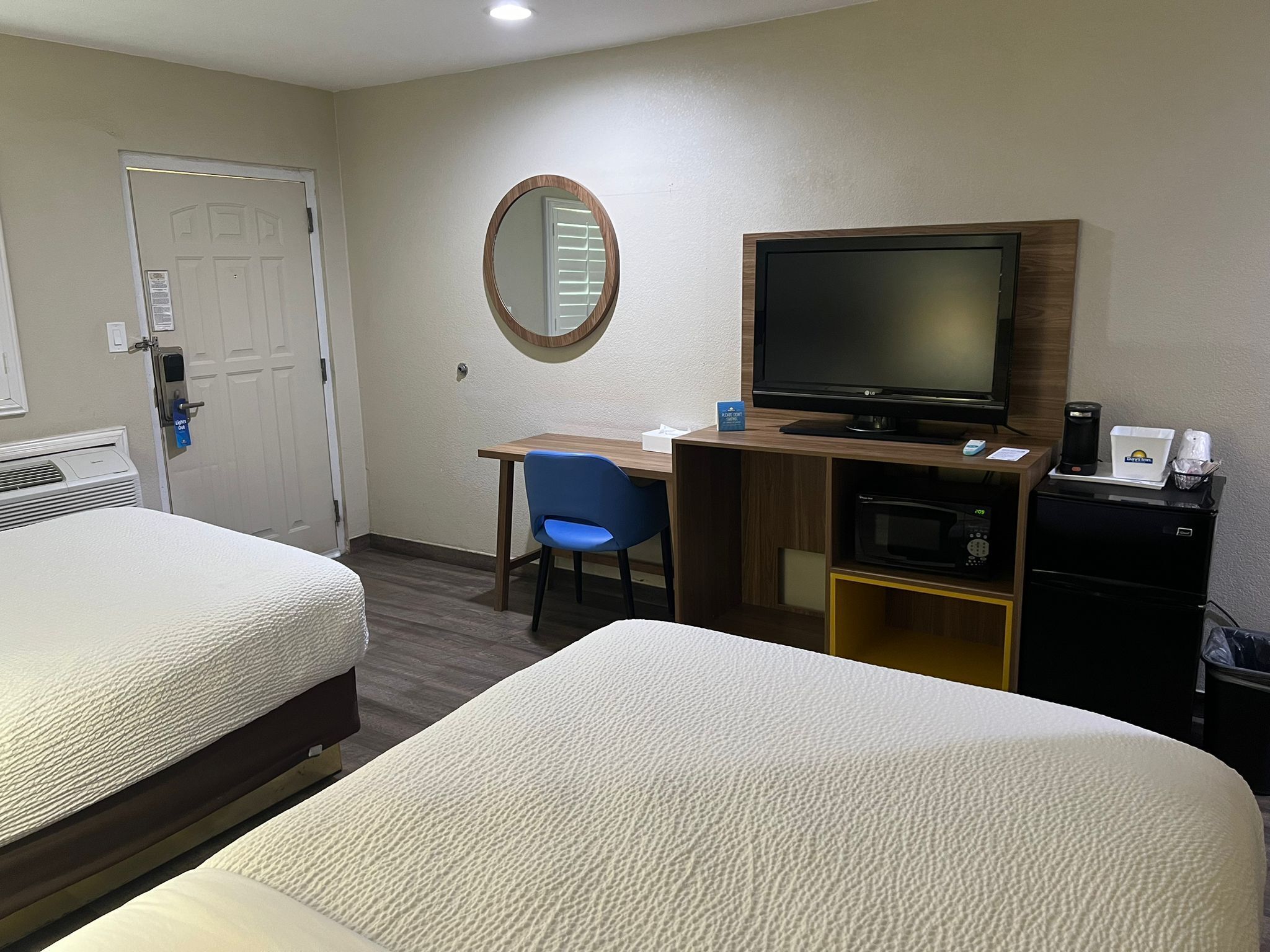 A hotel room with two beds, a desk with a chair, a television, a coffee maker, and a microwave.