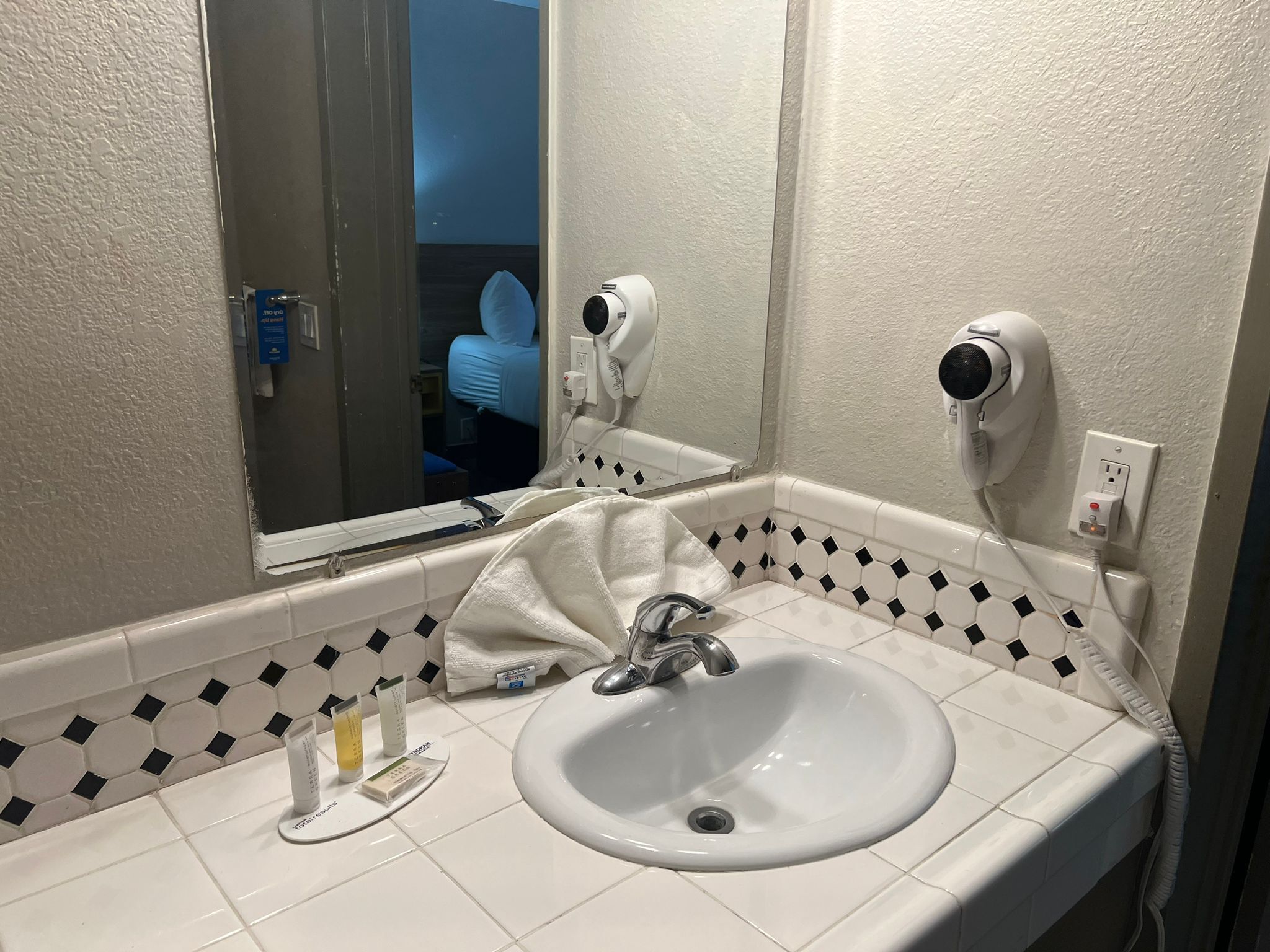 Uma casa de banho com uma pia branca, um espelho, uma toalha e um secador de cabelo.