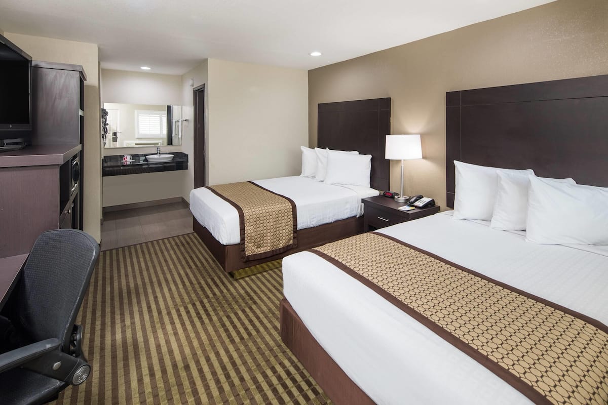 A hotel room with two beds, a desk, a chair, a TV, a mirror, and a bathroom visible in the background.
