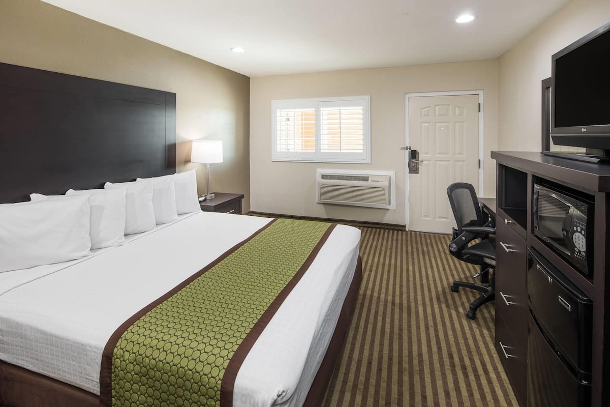 A hotel room with a large bed, a desk with a computer, a television, and a window with blinds.