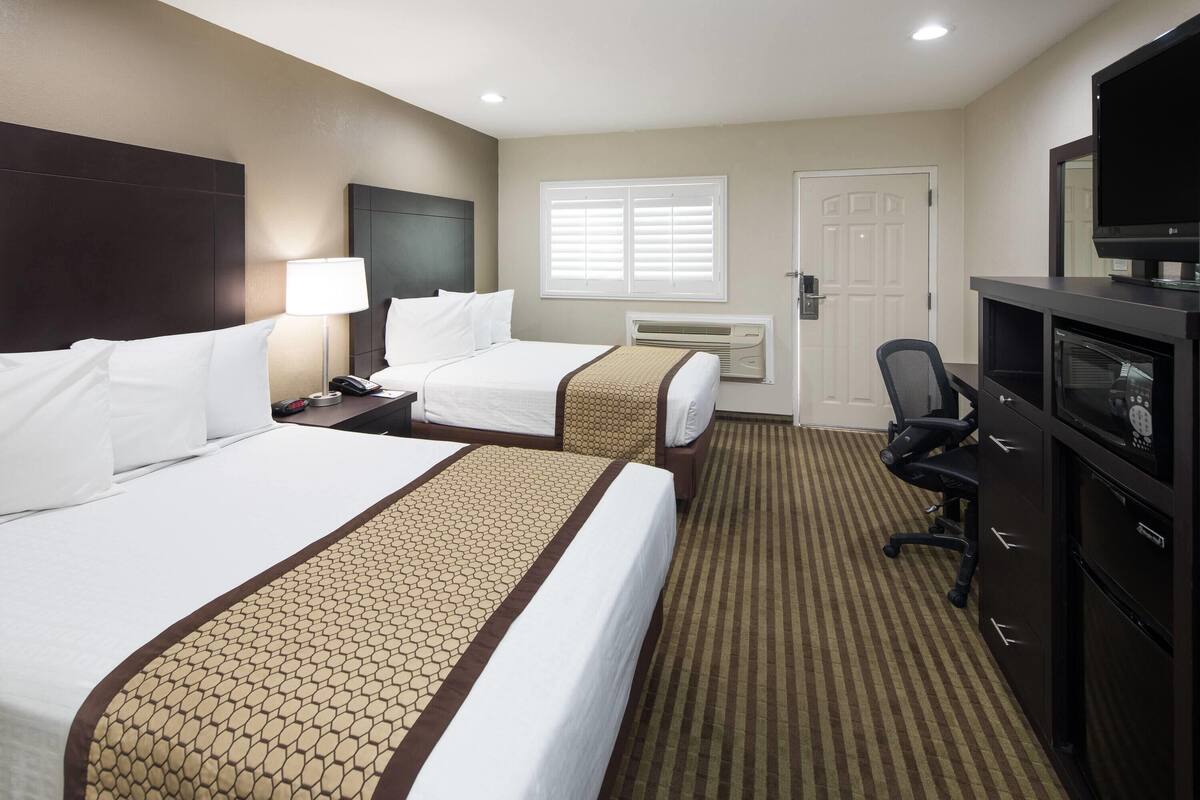 A hotel room with two beds, a desk, a chair, a television, and a door.