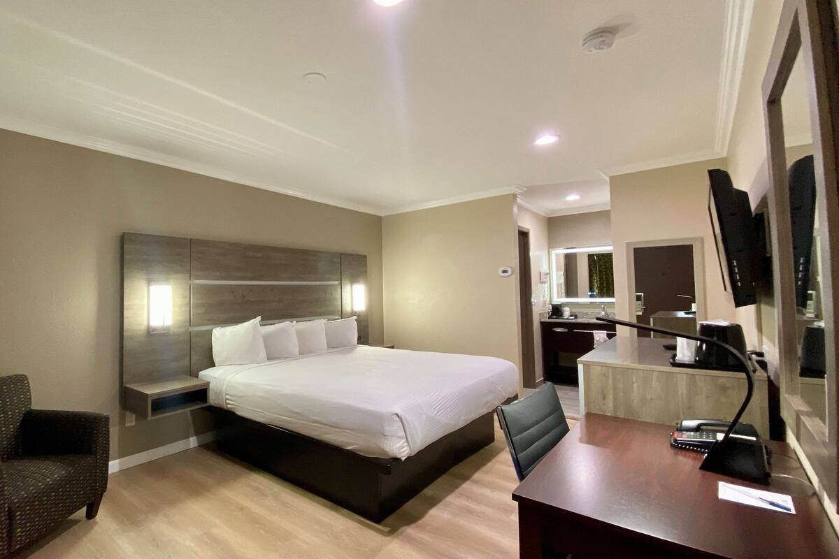 Habitación de hotel con una cama grande, un escritorio con teléfono, una silla, un pequeño sofá y un espejo.