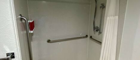 A small, enclosed shower area with a white shower curtain, a handheld showerhead, a grab bar, and a toilet with a white seat cover.