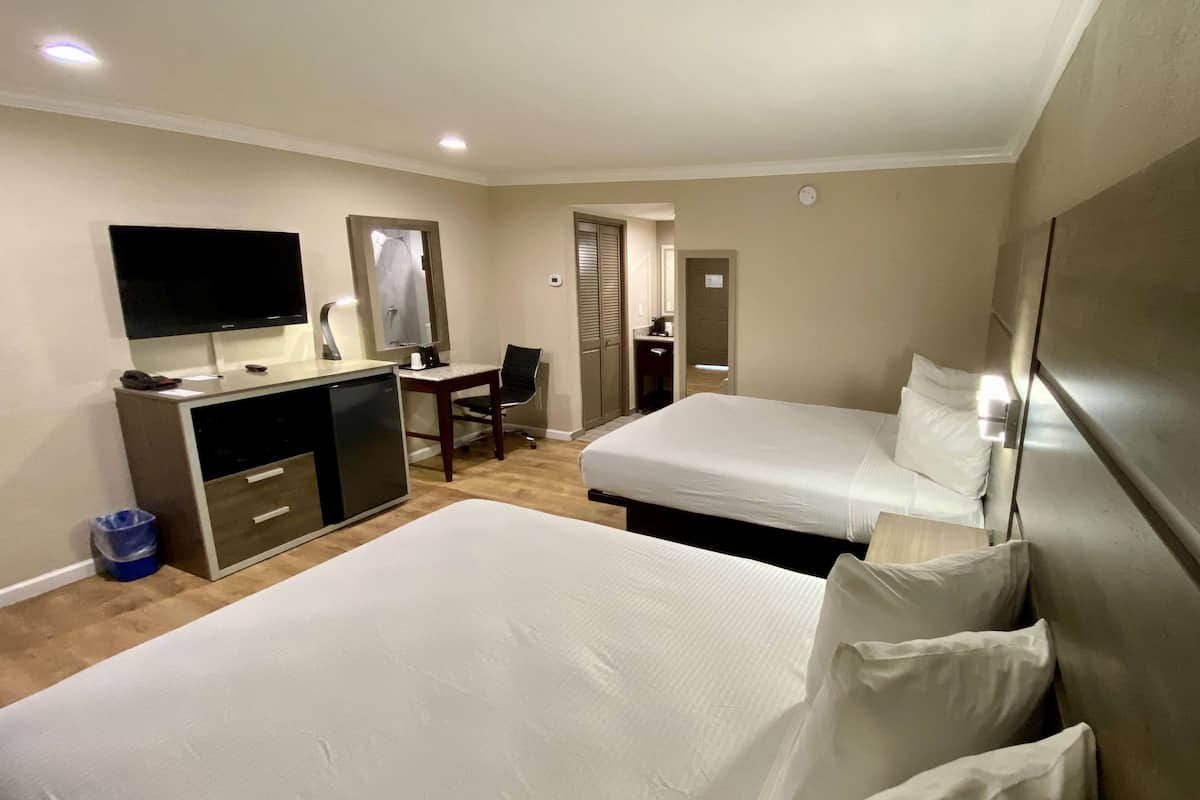 Habitación de hotel con dos camas, un escritorio con silla, televisor y baño visible a través de una puerta.