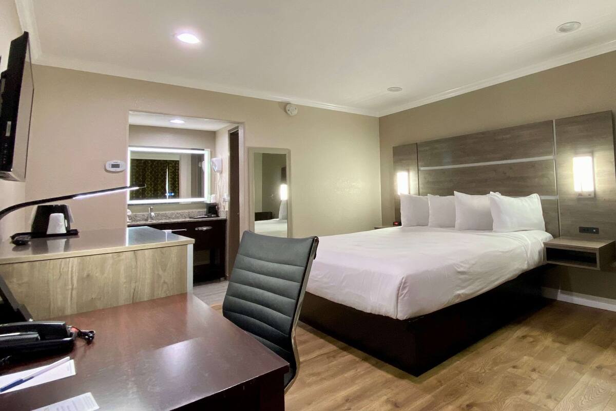 Una habitación de hotel con una cama, un escritorio, una silla, un televisor y un espejo.