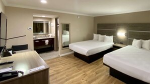 A hotel room with two beds, a desk with a telephone and papers, a mirror, and a bathroom with a sink and towel rack. - SureStay Hotel by Best Western Santa Cruz (Santa Cruz)
