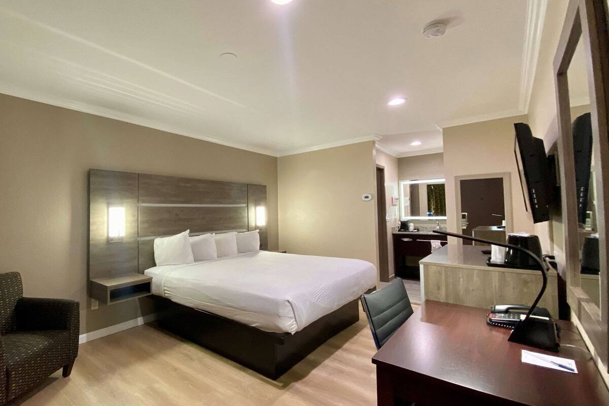 Habitación de hotel con cama, escritorio, silla, televisor y baño a la vista.