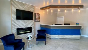 A reception area with a modern design, including a reception desk, two blue chairs, a flat-screen TV, and a wall-mounted fireplace. - SureStay Hotel by Best Western Santa Cruz (Santa Cruz)