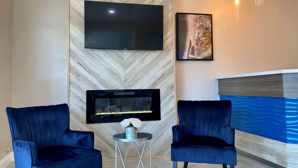 A modern room with a large flat-screen TV mounted on a marble wall, two dark blue armchairs, a small round table with a vase of flowers, and a framed picture above the TV. - SureStay Hotel by Best Western Santa Cruz (Santa Cruz)