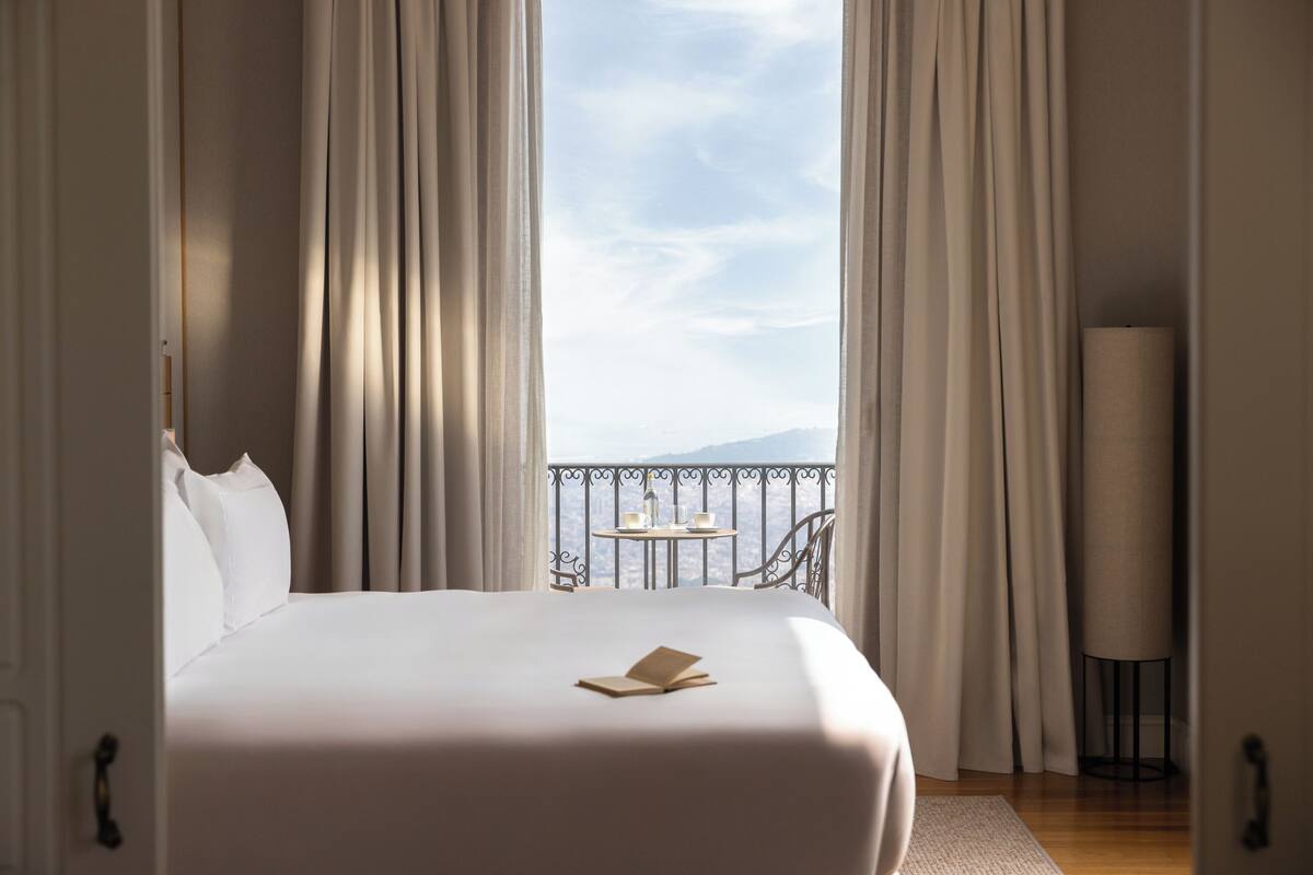 Quarto de hotel com cama grande, vista para o mar e varanda com mesa e cadeiras.