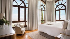 A hotel room with a large bed, a chair, a desk, and a view through arched windows. - METT Barcelona GL – A Leading Hotel of the World (Barcelona)