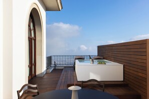 A balcony with a wooden floor, a white table with a chair, a small white bar area, and a view of the sky. - METT Barcelona GL – A Leading Hotel of the World (Barcelona)
