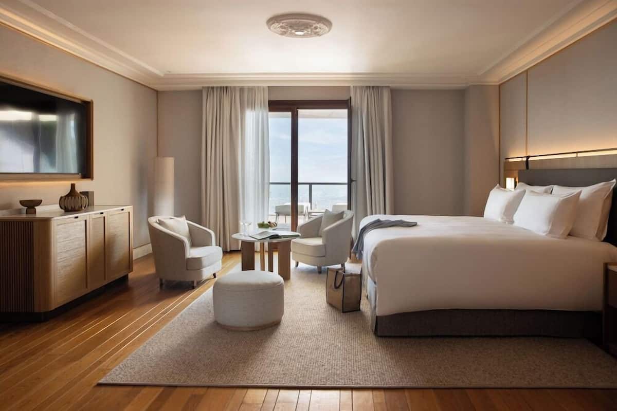 Quarto de hotel com uma cama grande, uma escrivaninha, uma cadeira, uma televisão e vista para o exterior.