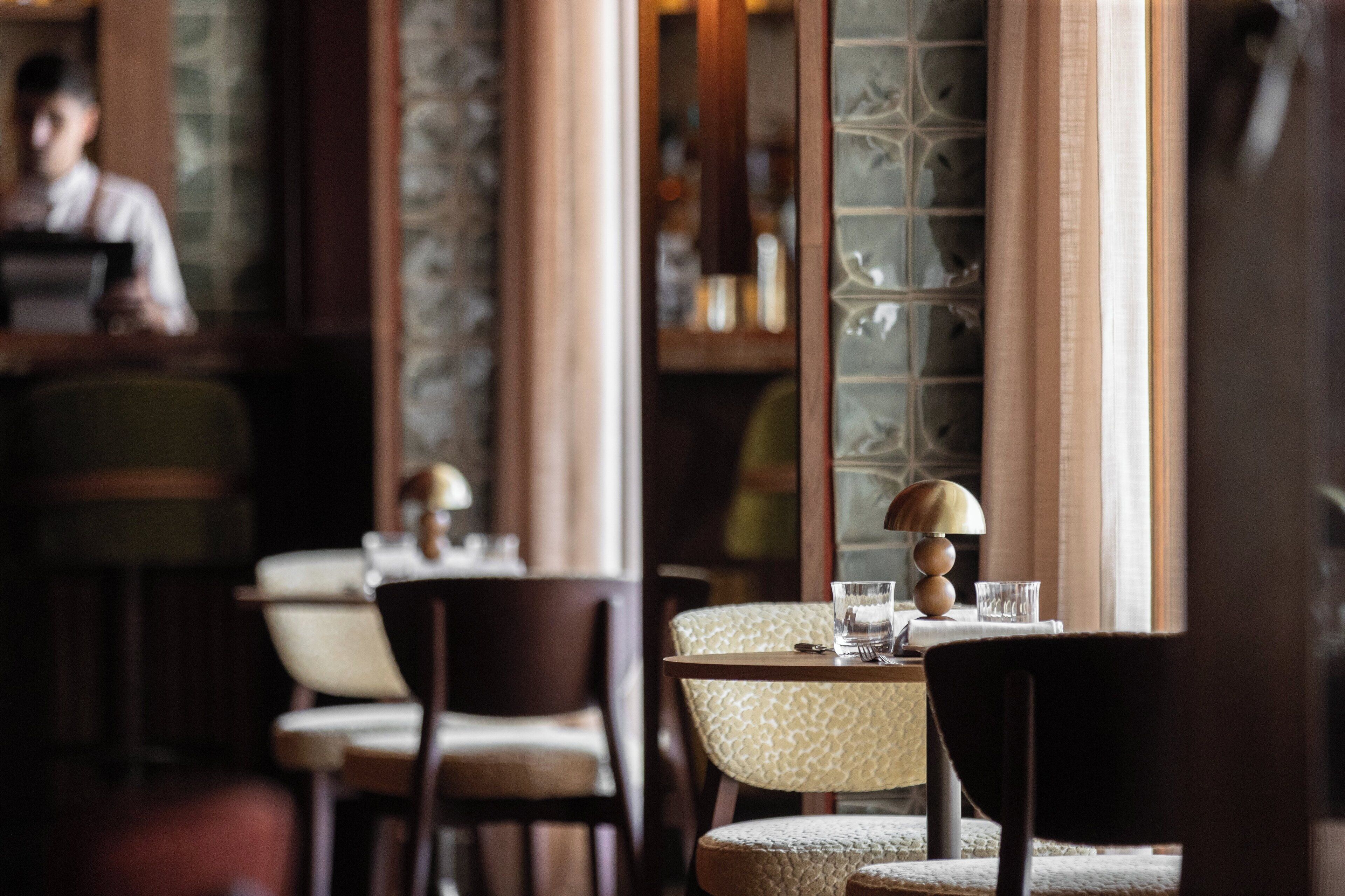 Een restaurantinterieur met een bar, tafels met stoelen en een behangetapijt.