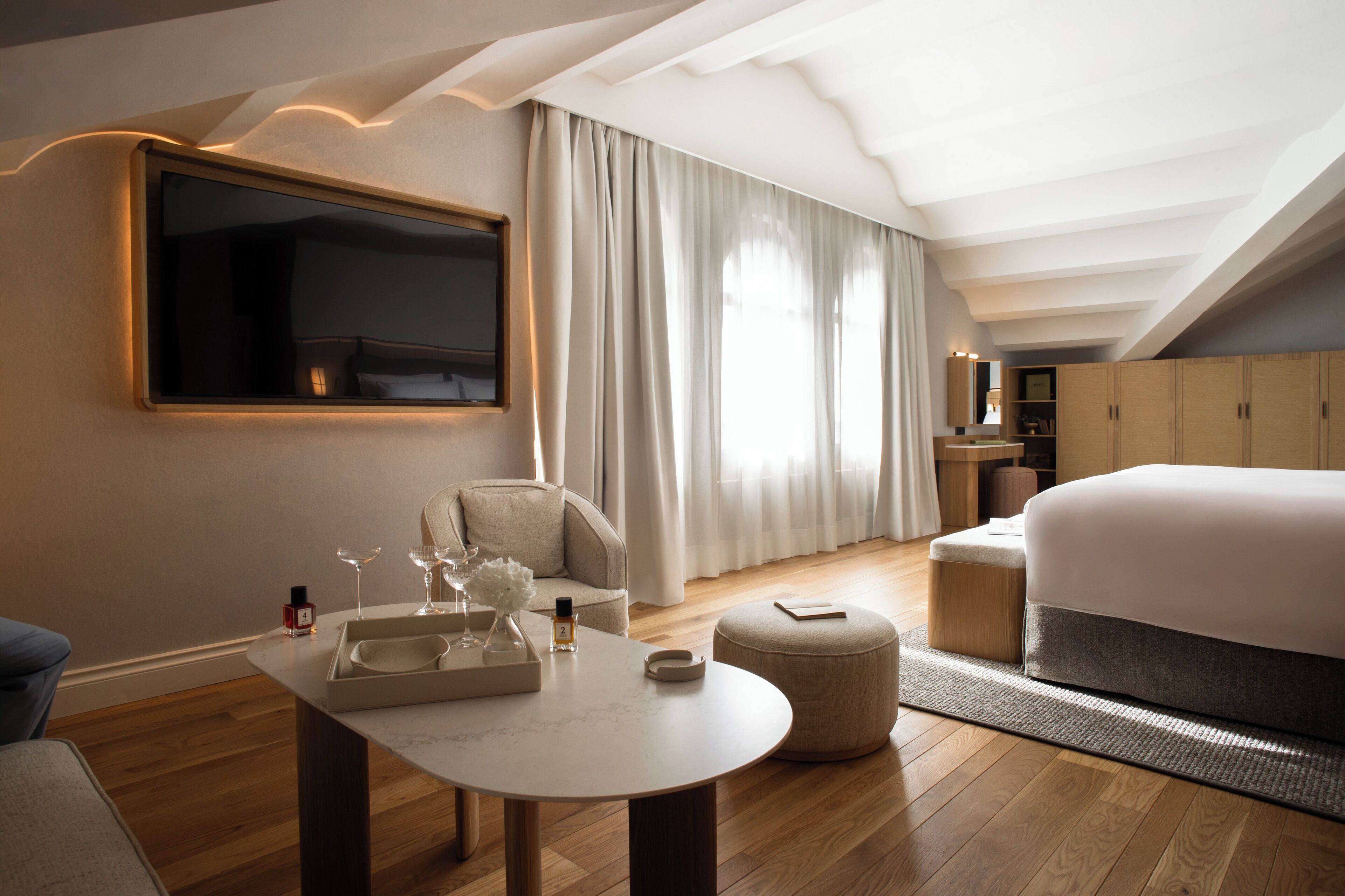 A modern hotel room with a large bed, a seating area with a table, and a TV mounted on the wall.