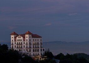 Un edificio de varios pisos con techo de tejas rojas, múltiples balcones y vistas del paisaje circundante.