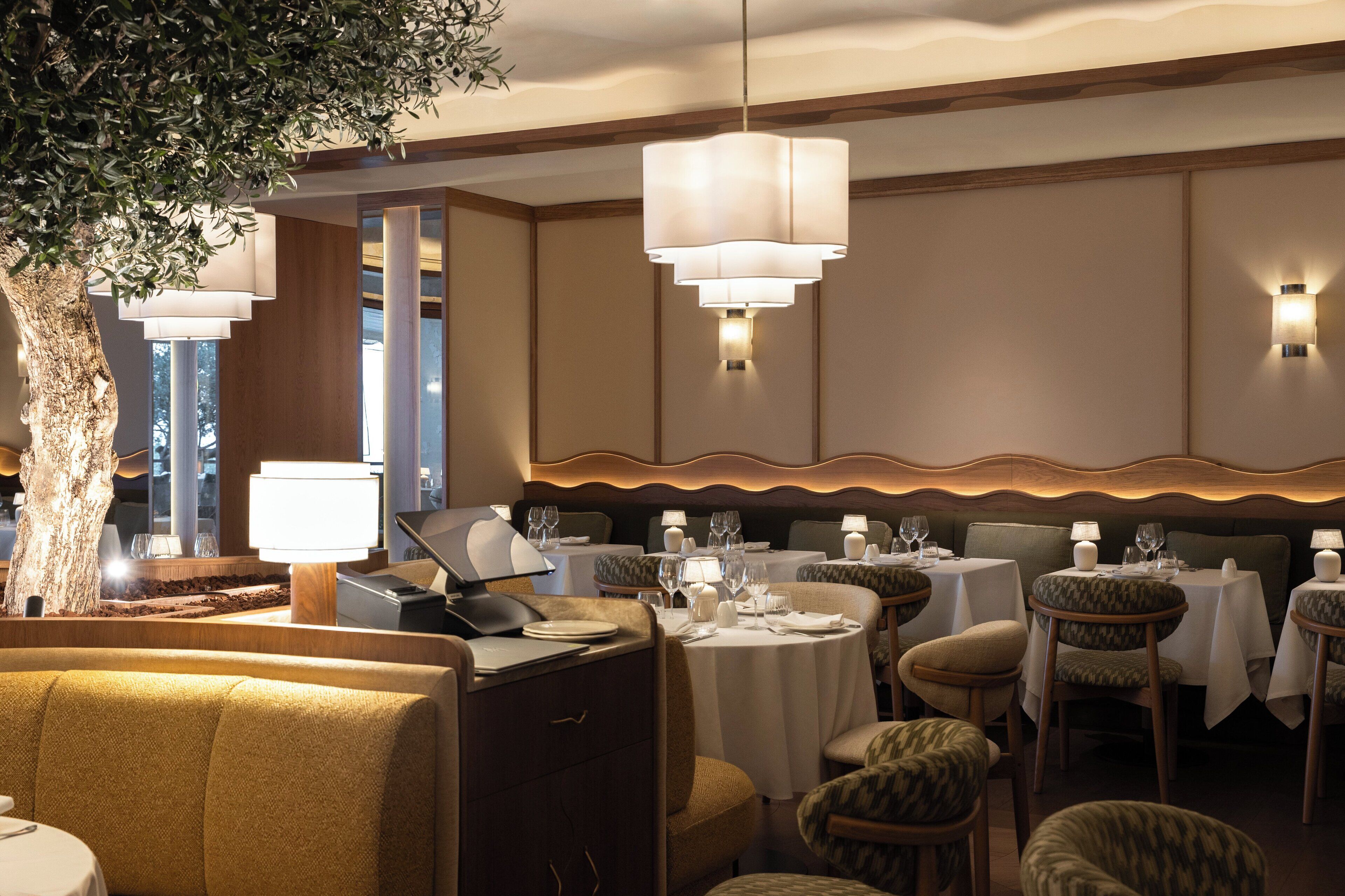 Un restaurant avec des tables rondes, des chaises et un arbre en arrière-plan.