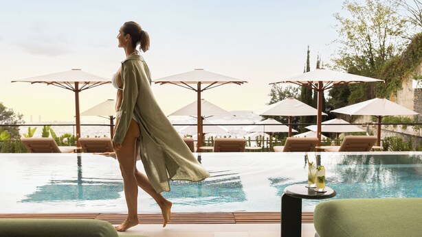 A woman walking by a poolside with lounge chairs and umbrellas. - METT Barcelona GL – A Leading Hotel of the World (Barcelona)