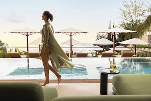 Una mujer caminando cerca de una piscina con sillones de descanso y sombrillas.