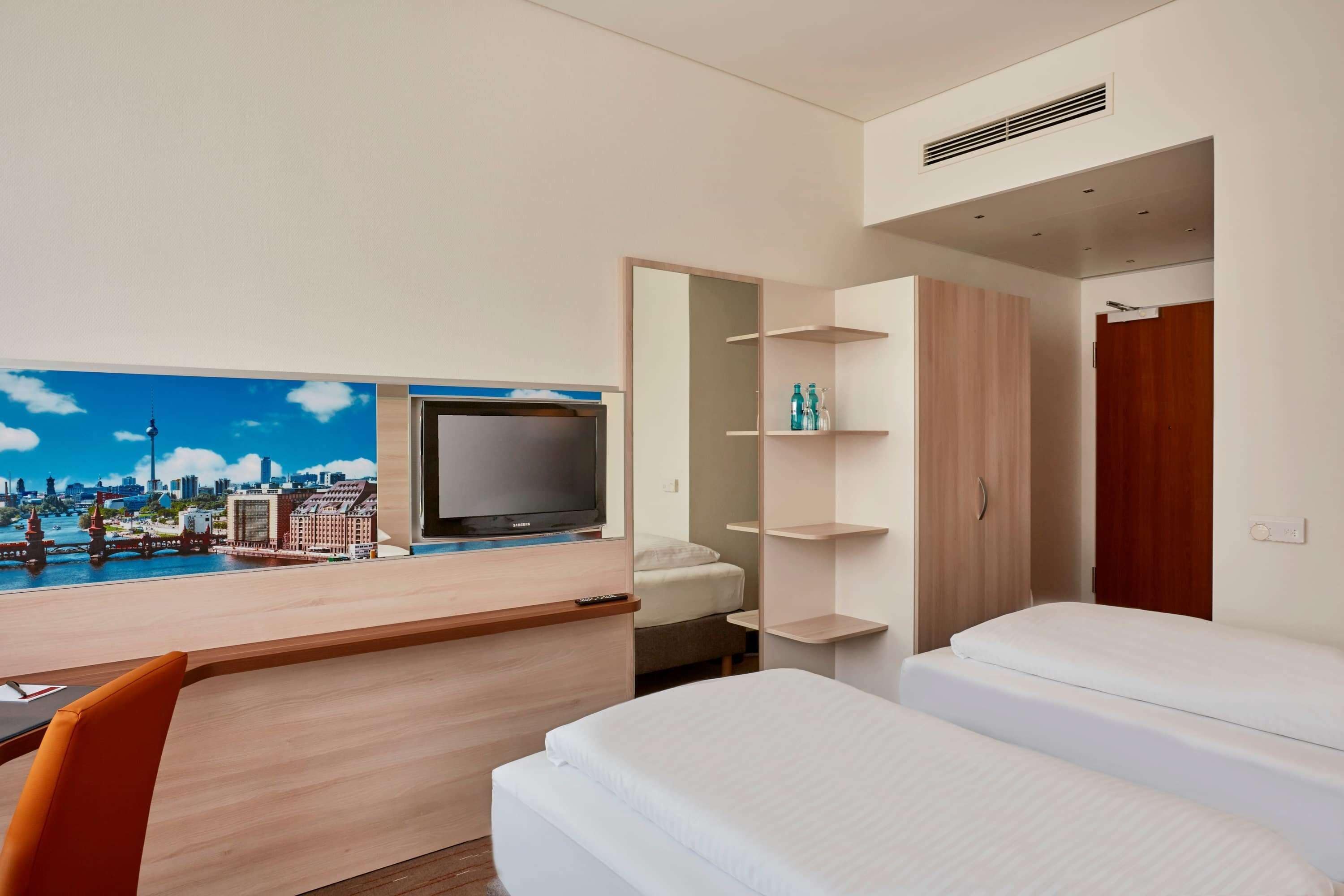 Habitación de hotel con cama, escritorio con televisor, un mural de paisaje urbano y un armario.