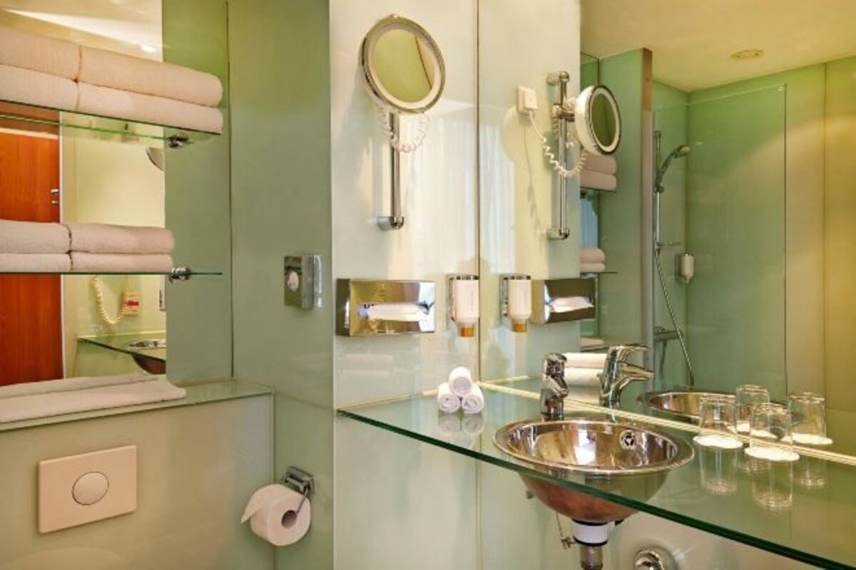 Un baño moderno con un lavabo de vidrio, dos espejos, un espejo de mano y una cabina de ducha de vidrio.