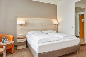 Una camera d'hotel con un letto, due comodini, una sedia e un tavolino con bottiglie.