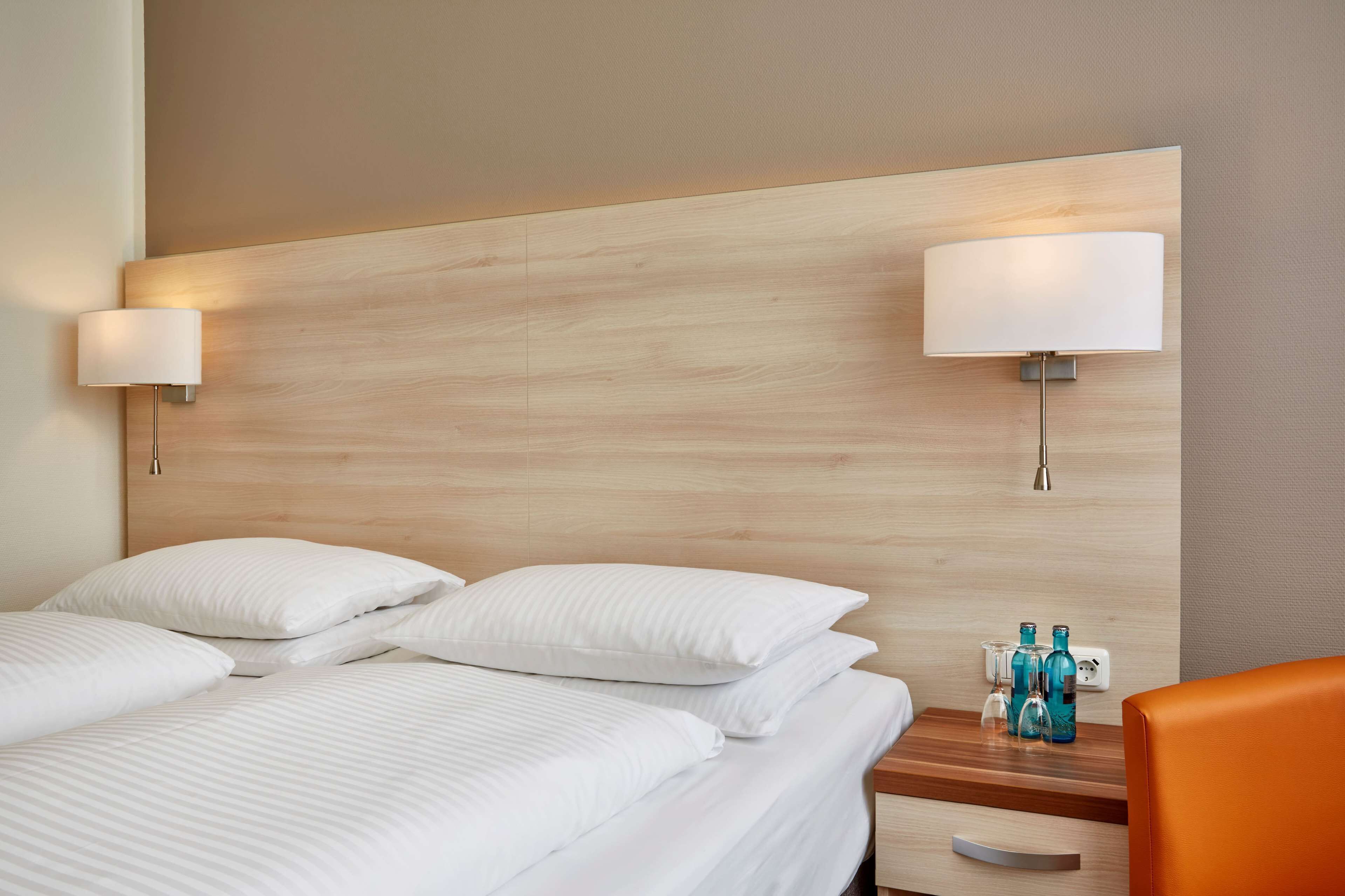 Quarto de hotel com duas camas, painel de cabeceira de madeira, abajures e uma mesinha com garrafas.