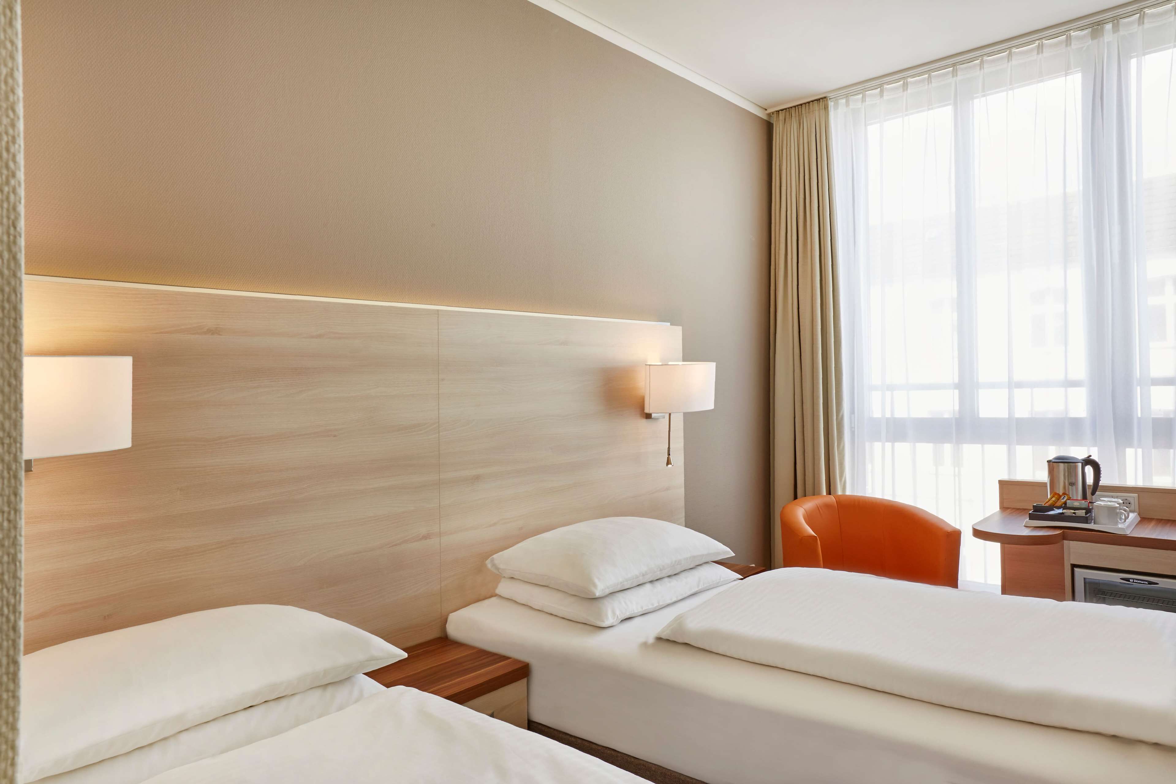 Une chambre d’hôtel avec deux lits, une tête de lit en bois, un bureau avec une machine à café et une chaise.