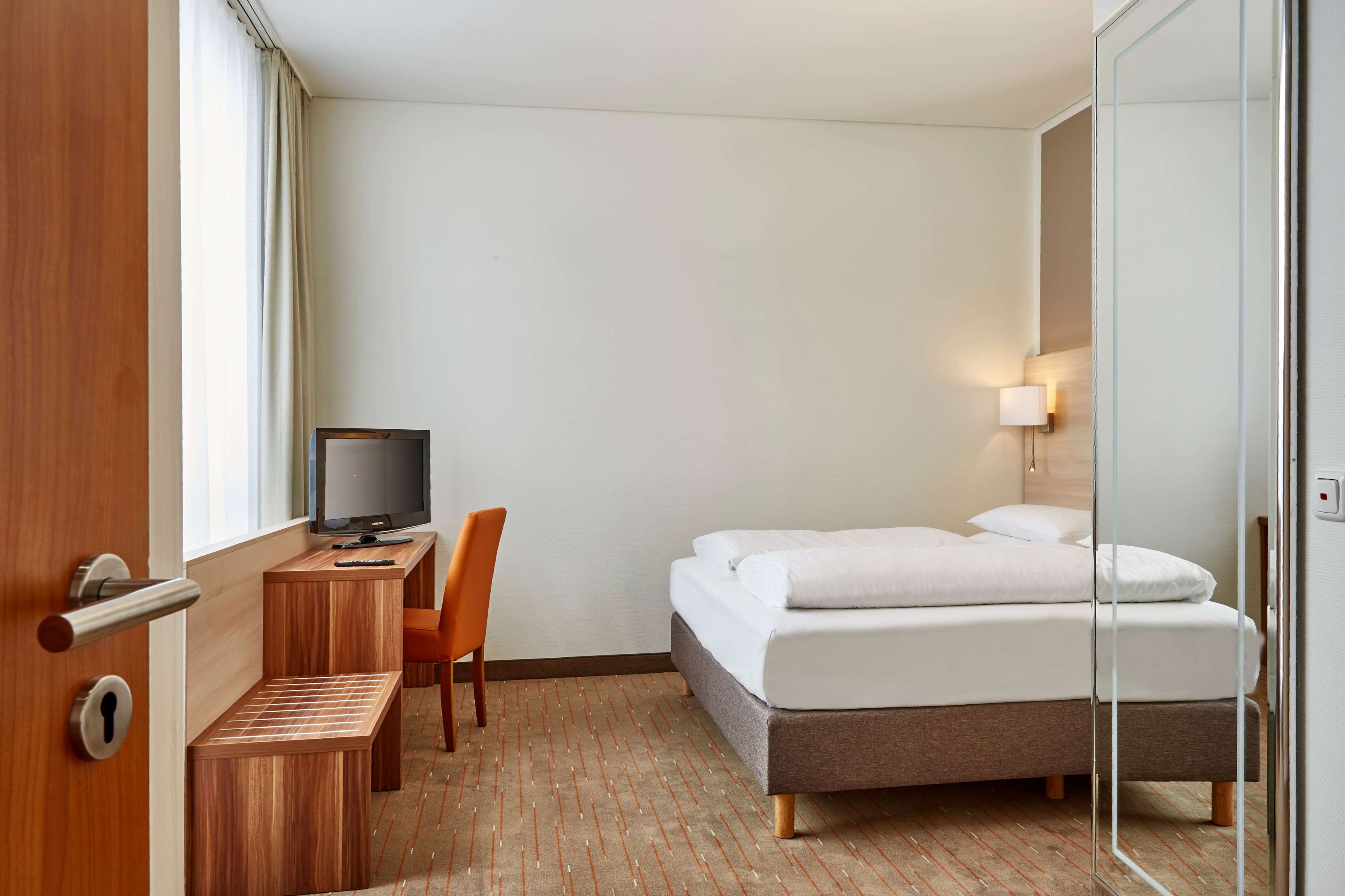 Een hotelkamer met een bed, een bureau met stoel, een televisie en een raam met gordijnen.