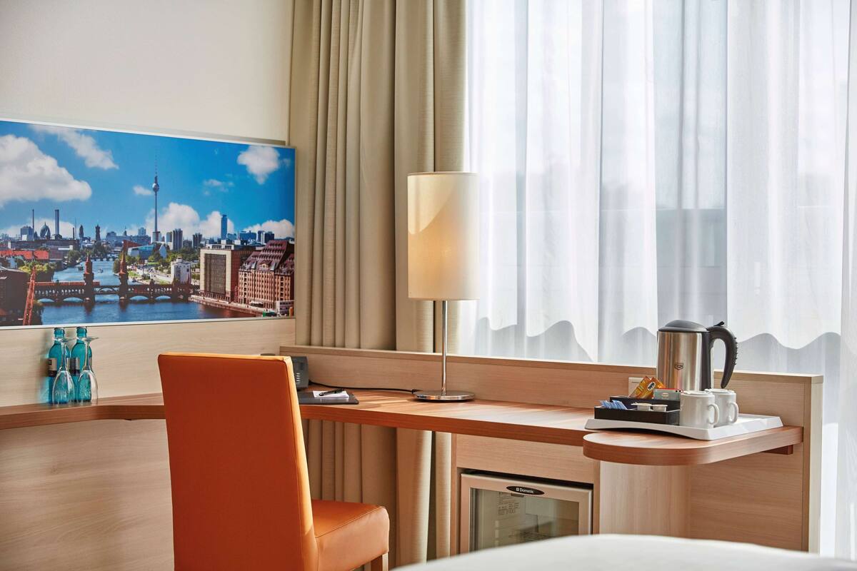 A hotel room with a desk, a chair, a lamp, a coffee maker, and a view of a cityscape.