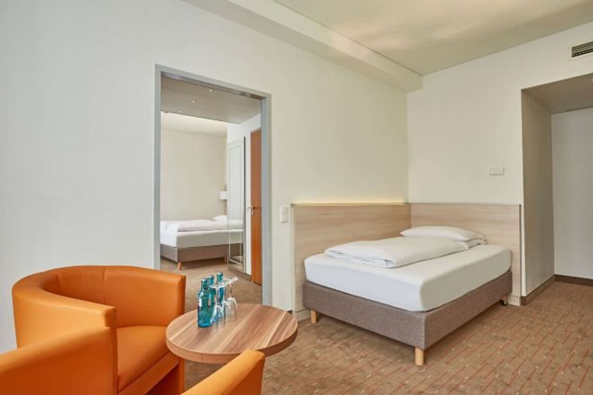 Una habitación de hotel con una cama, una mesa redonda de madera y sillas, y una silla naranja brillante.