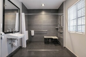 A modern bathroom with a shower, a sink, a mirror, and a window with blinds.