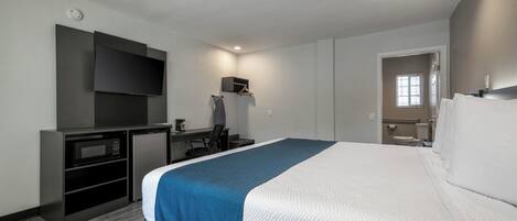 A hotel room with a bed, a desk with a flat-screen TV, a microwave, and a small kitchenette.