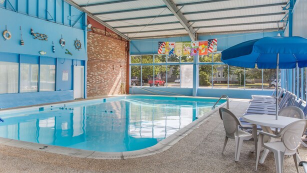 An indoor swimming pool with a covered area, poolside chairs, and a table. - Americas Best Value Inn & Suites Hyannis Cape Cod (Hyannis)
