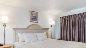 A hotel room with a large bed, two bedside lamps, a nightstand, a framed picture on the wall, and a curtain. - Americas Best Value Inn & Suites Hyannis Cape Cod (Hyannis)