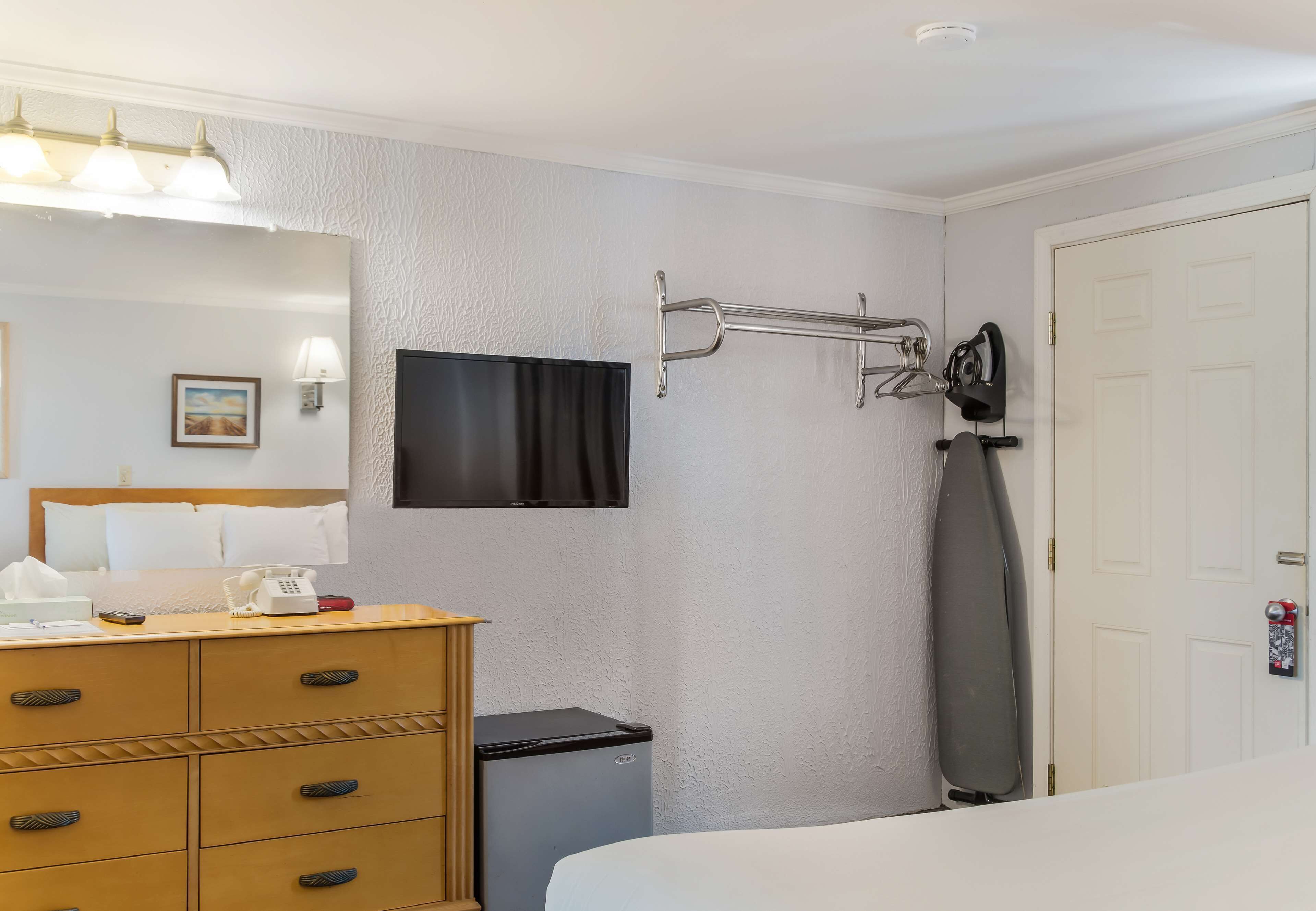 Een hotelkamer met een bed, een dressoir, een bureau, een televisie, een kapstok en een deur.