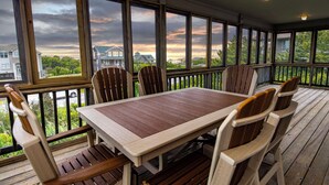 A wooden deck with a table and chairs, large windows with a view of houses and trees, and a railing. - The Sanderling (Duck)