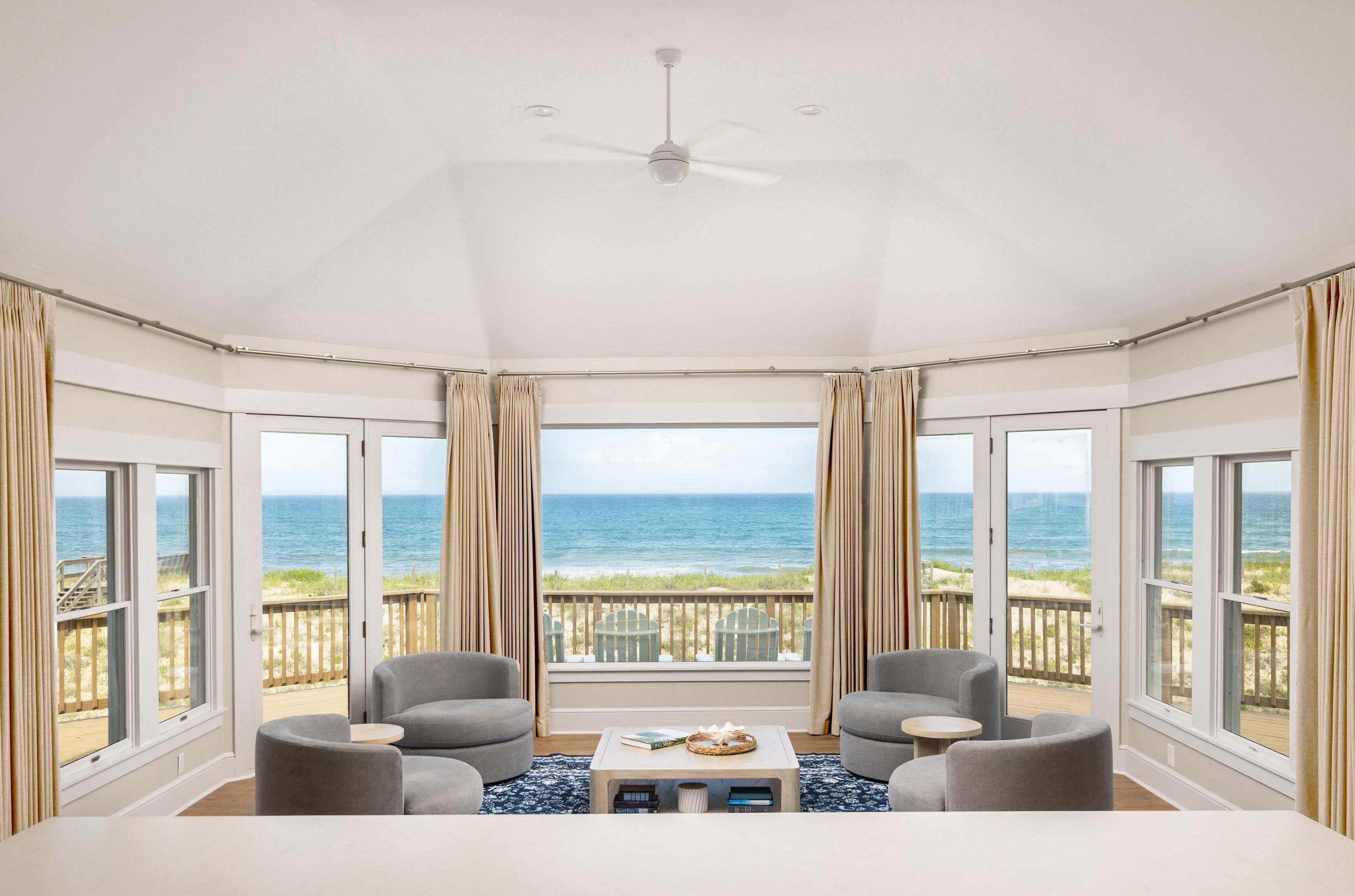 A room with a view of the ocean, a ceiling fan, and two armchairs.