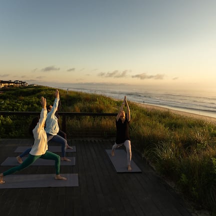 A yoga class on a wooden deck overlooking the ocean with a clear sky.