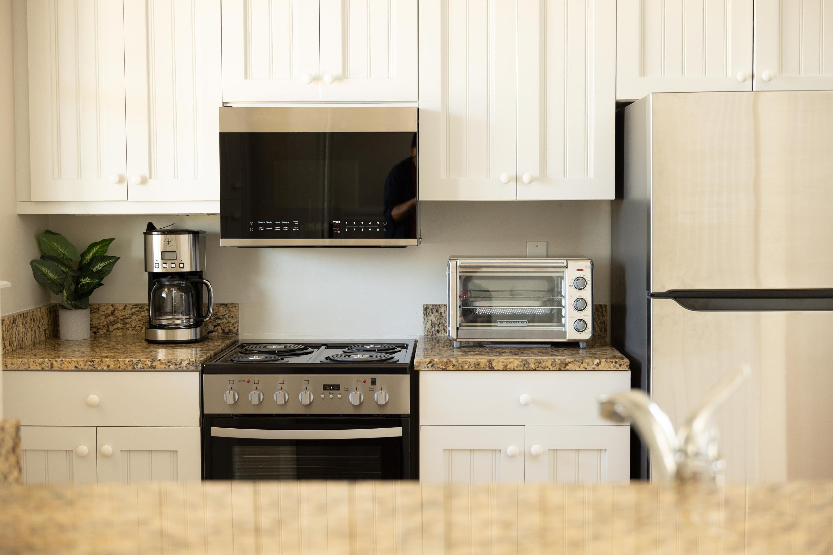 A kitchen with white cabinets, a stainless steel stove, a built-in oven, a microwave, a toaster, and a refrigerator.