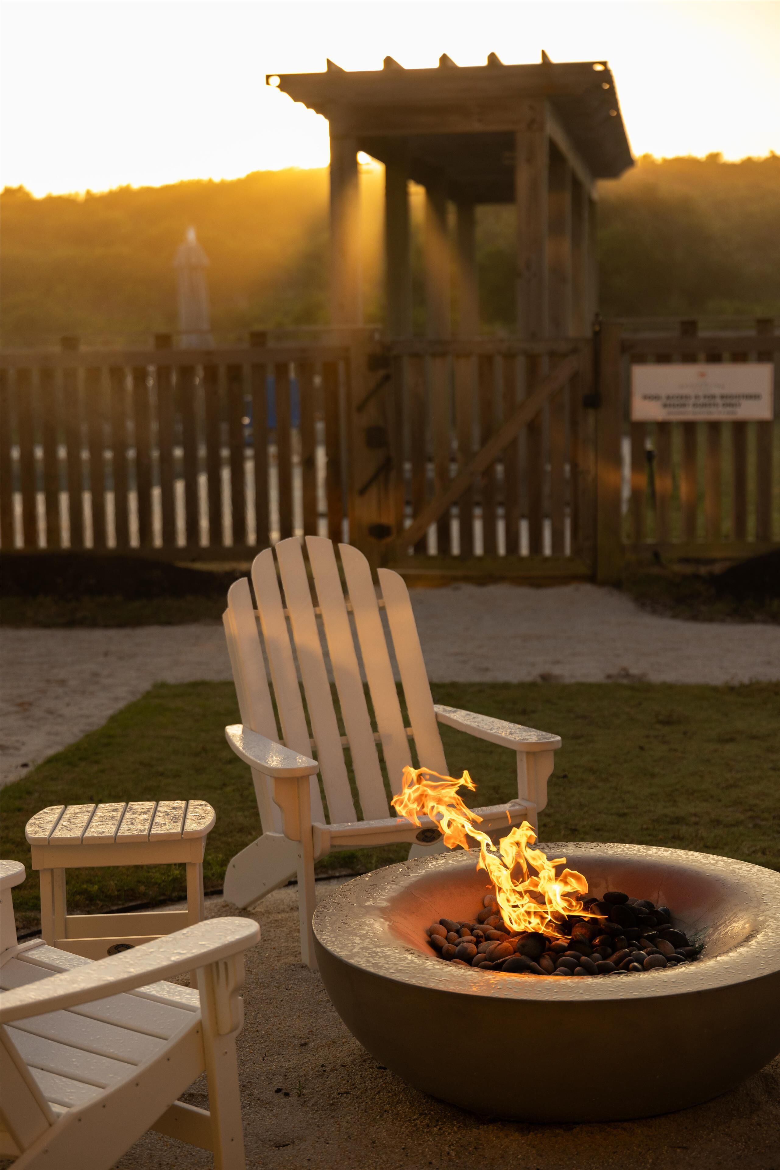 Une terrasse en bois avec des fauteuils Adirondack et un foyer où brûle du bois.