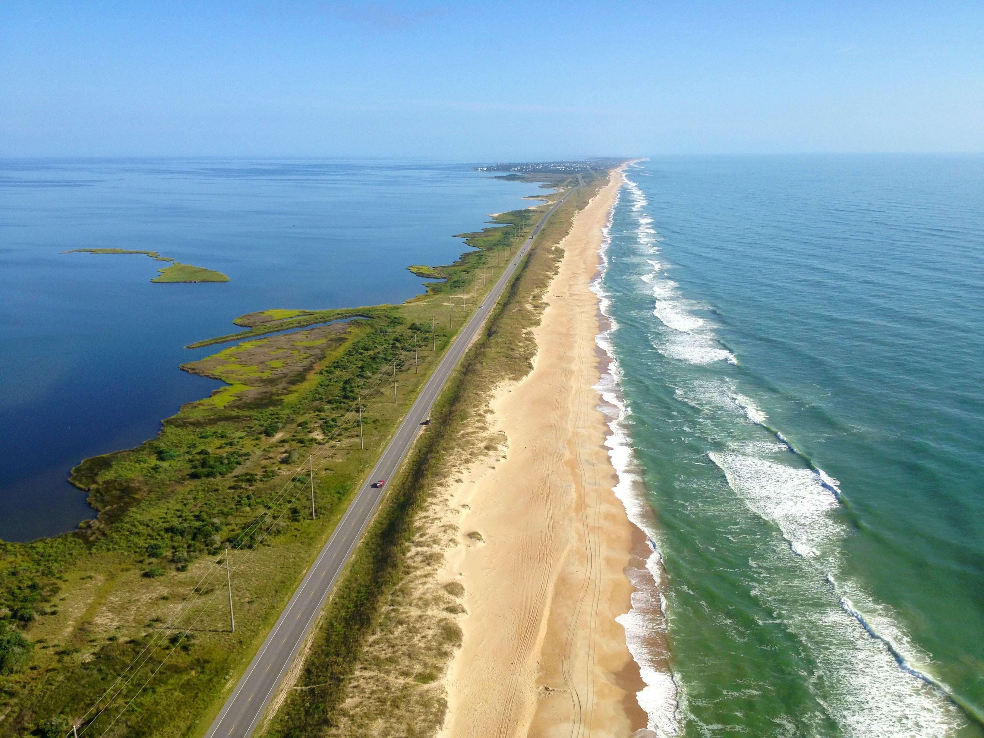 A coastal road with a beach on one side and a body of water on the other.