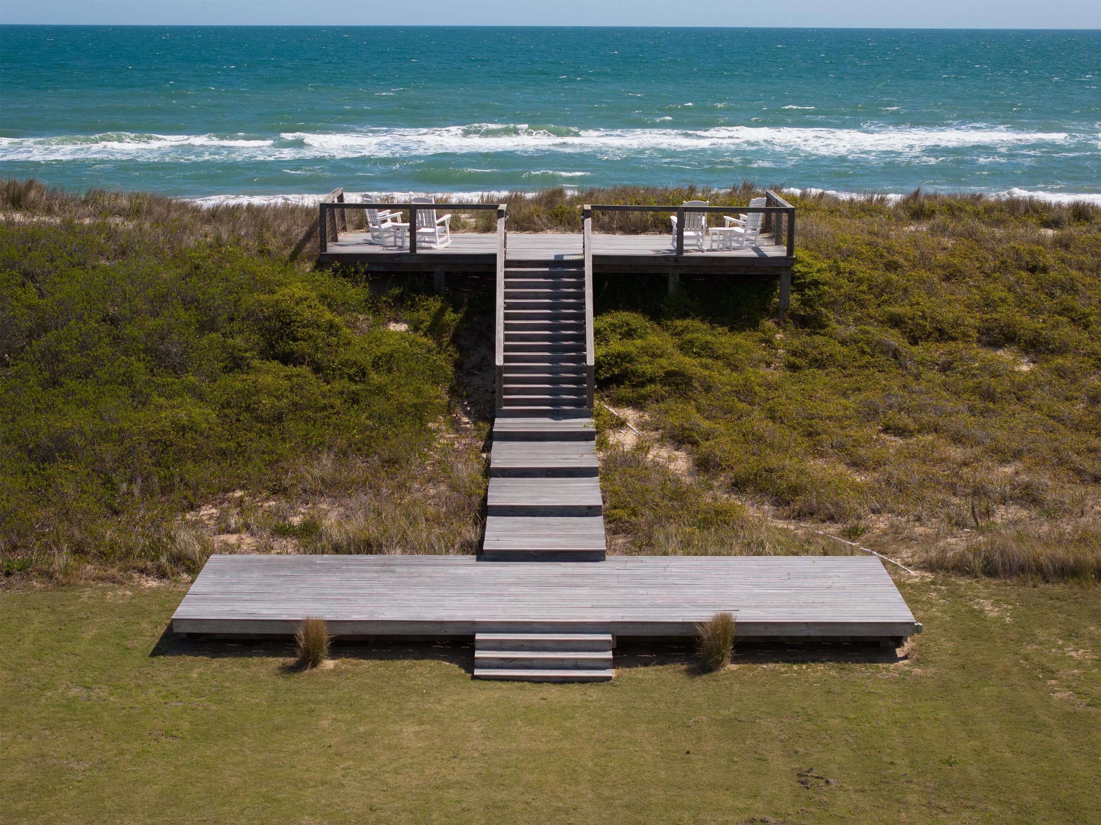 A wooden boardwalk leading to a deck with chairs overlooking the ocean.
