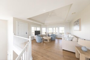 A spacious living room with a white staircase, a round wooden coffee table, and a beige sofa.