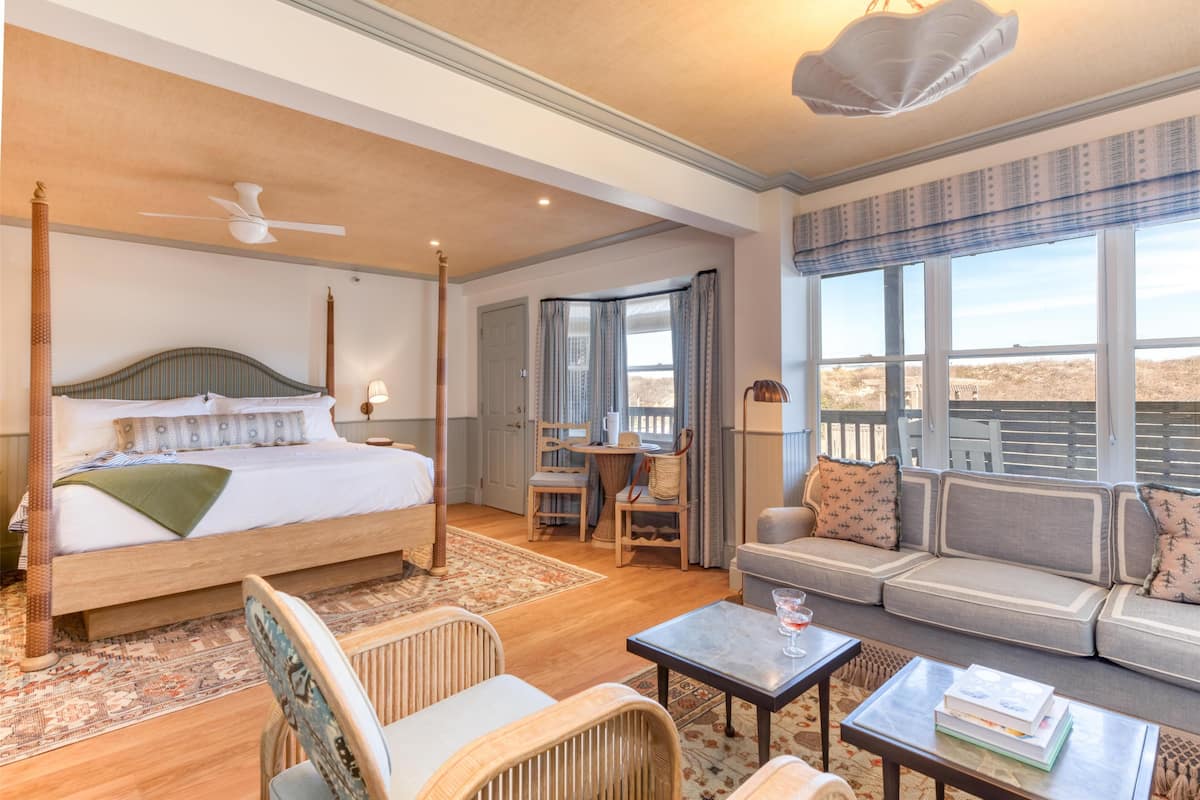 Une chambre à coucher avec un lit à baldaquin, un coin salon avec un canapé et des fauteuils, et une vue sur le désert grâce à de grandes fenêtres.