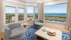 A balcony with a view of the ocean, a seating area with chairs, and a table with a book and decorative item.