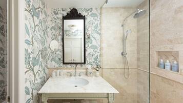 A bathroom with a marble sink, a large mirror, a shower, and a shelf with toiletries.